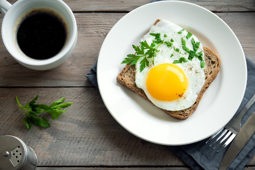 A nutritious breakfast scene with a fried egg on toast, seasoned and garnished with parsley, accompanied by a cup of coffee on the table.