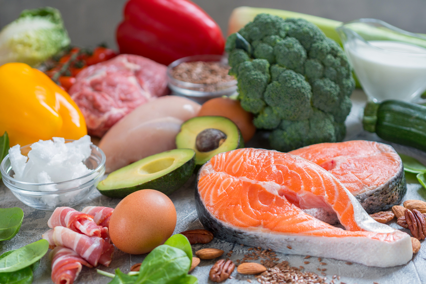 A variety of meal plan ingredients spread out on a table including fish, meat, vegetables, nuts, milk, and cereals.