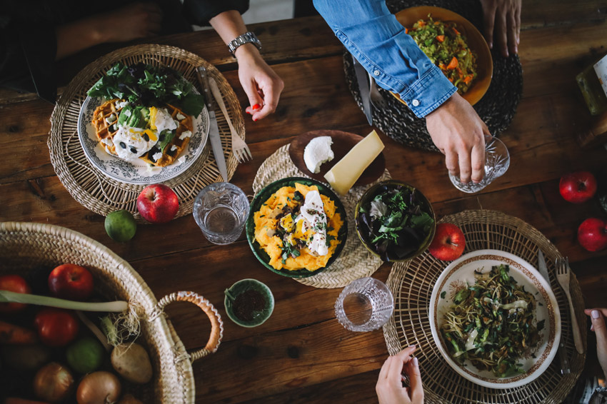 People enjoying a variety of healthy dishes at a table with fresh fruits and vegetables placed around.