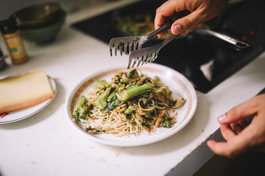 Plating a colourful, healthy noodle and vegetable dish in a kitchen, next to an electric stovetop.