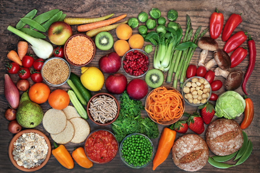 Colourful healthy foods including fruits, vegetables, bread, and legumes on a table.