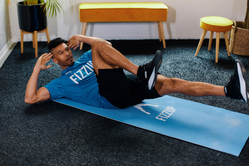Man doing cross crunches on a mat at home in FizzUp workout gear.