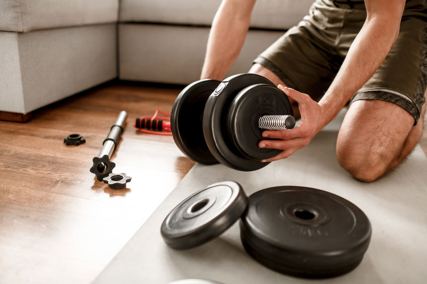 Man adding weight plates to an adjustable dumbbell in his living room.