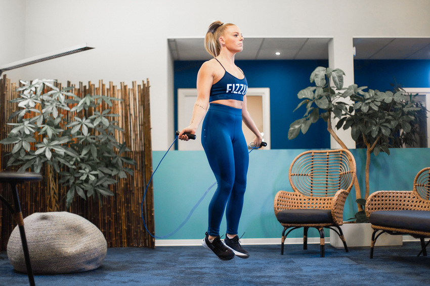 Fit young woman wearing FizzUp sportswear jumping rope indoors, focused on her workout.