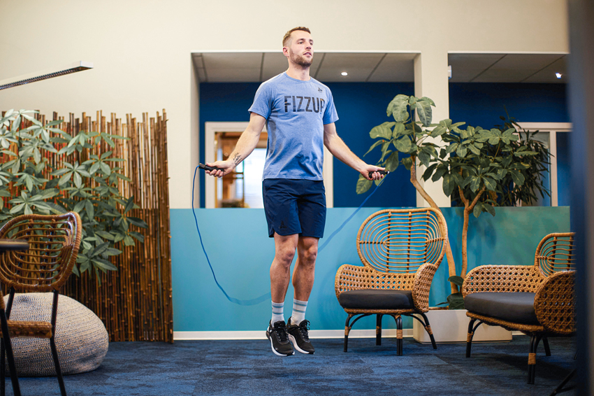 Fit young man wearing FizzUp sportswear jumping rope indoors, focused on his workout.