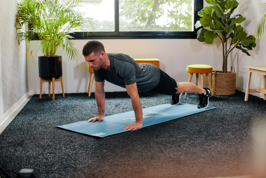 Man doing straight arm plank exercise at home on mat.