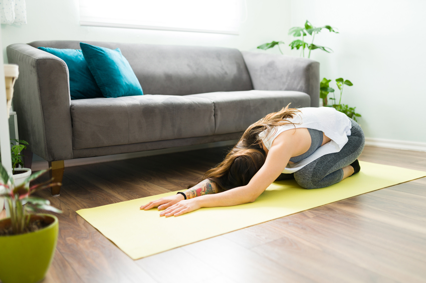 Woman stretching on yoga mat at home, child pose exercise.